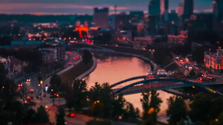 A panoramic sunset view of the Vilnius city skyline with a river and bridges.