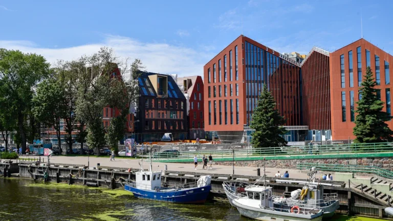 Traditional fishing boats docked in Klaipeda, Lithuania, with modern brick buildings along the sunlit waterfront.