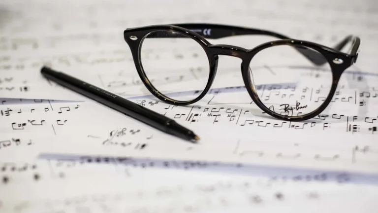 Black framed glasses and a ballpoint pen resting on top of handwritten sheet music.