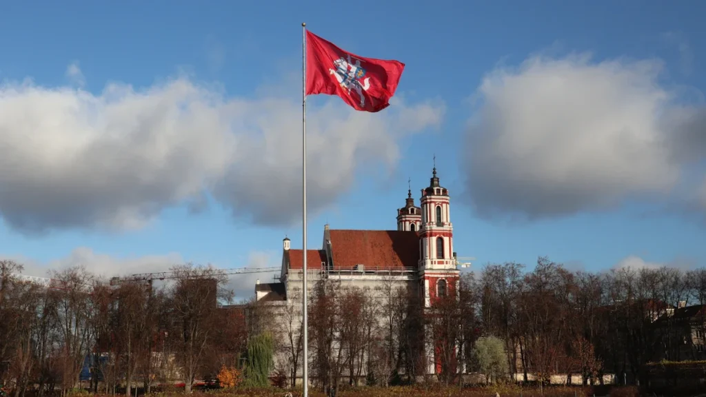 A red Lithuanian flag with a white knight flies in front of a historic building in Vilnius.