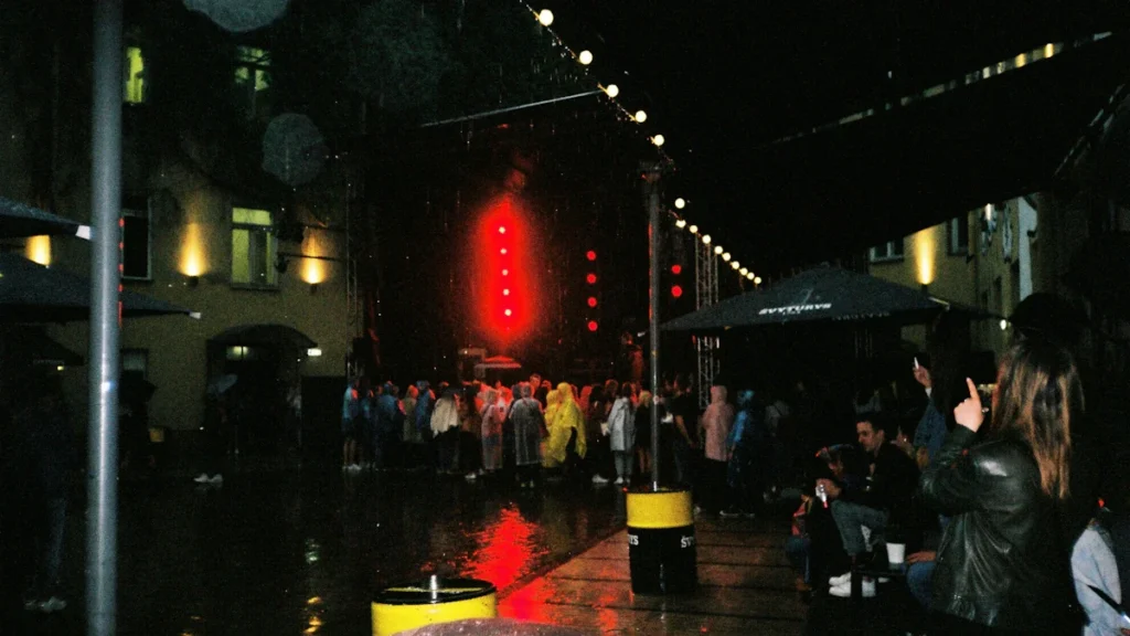 A large crowd gathers at an outdoor night event in Vilnius with stage lights and overhead decorations.