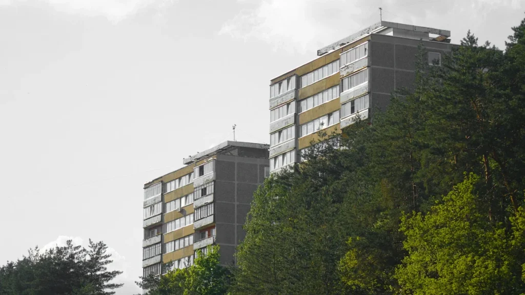 Modern residential apartment buildings with brown and white facades nestled among green trees in Vilnius, Lithuania.