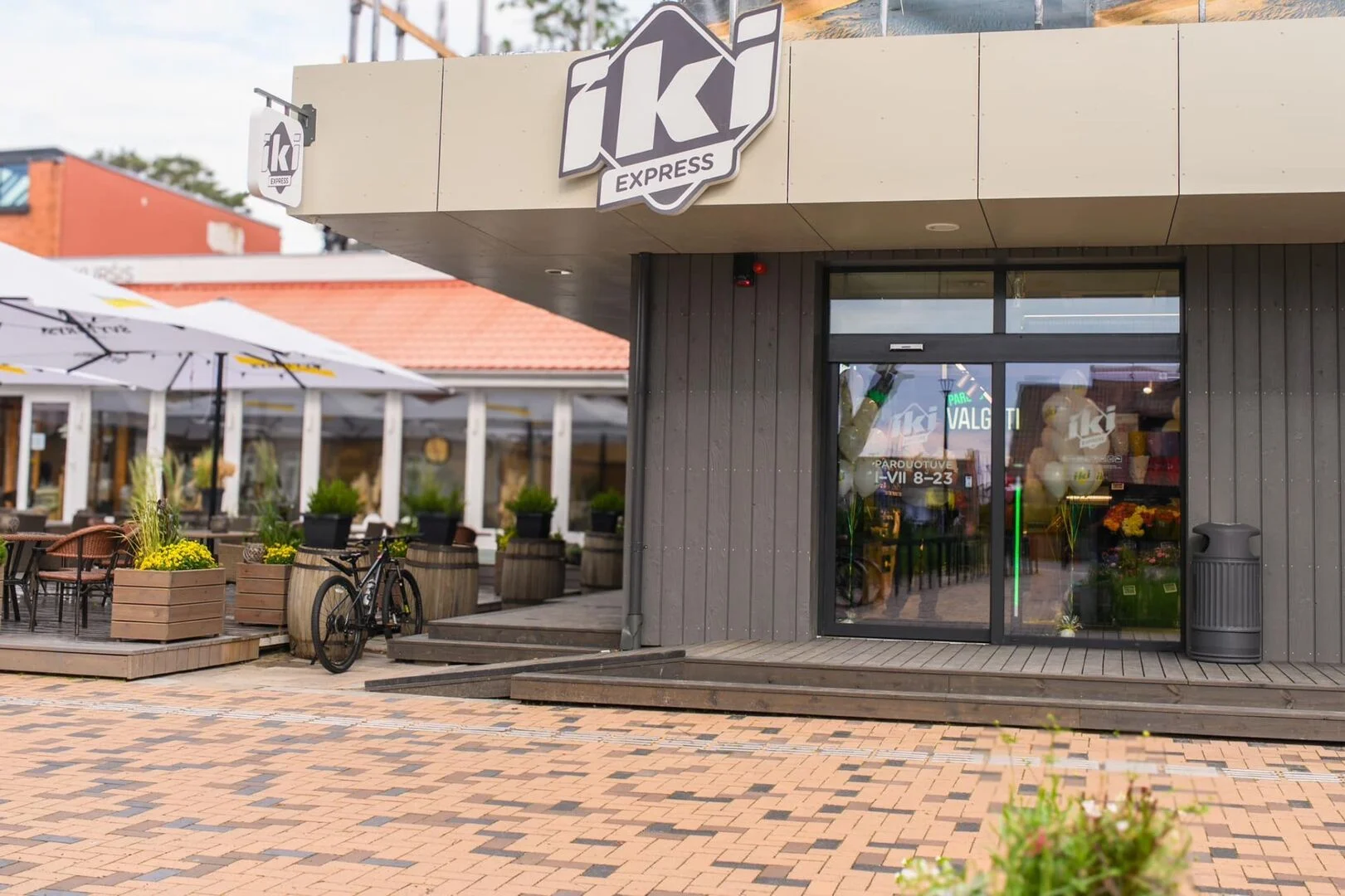Exterior view of an IKI Express grocery store entrance with wooden steps and a bicycle.