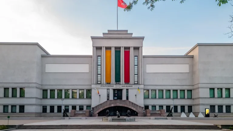 A grand, symmetrical stone building in Lithuania featuring large vertical banners in the national colors.