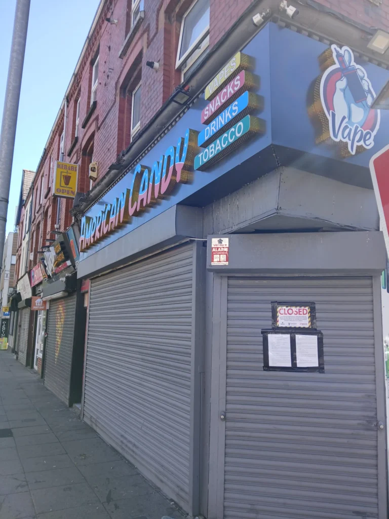 Storefront for American Candy with metal shutters pulled down and a closed notice attached.