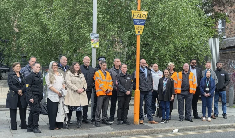A diverse group of people standing next to an orange Operation Halo help point sign outdoors.
