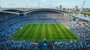 Wide shot of a packed Etihad Stadium with fans waving blue flags during a football match.