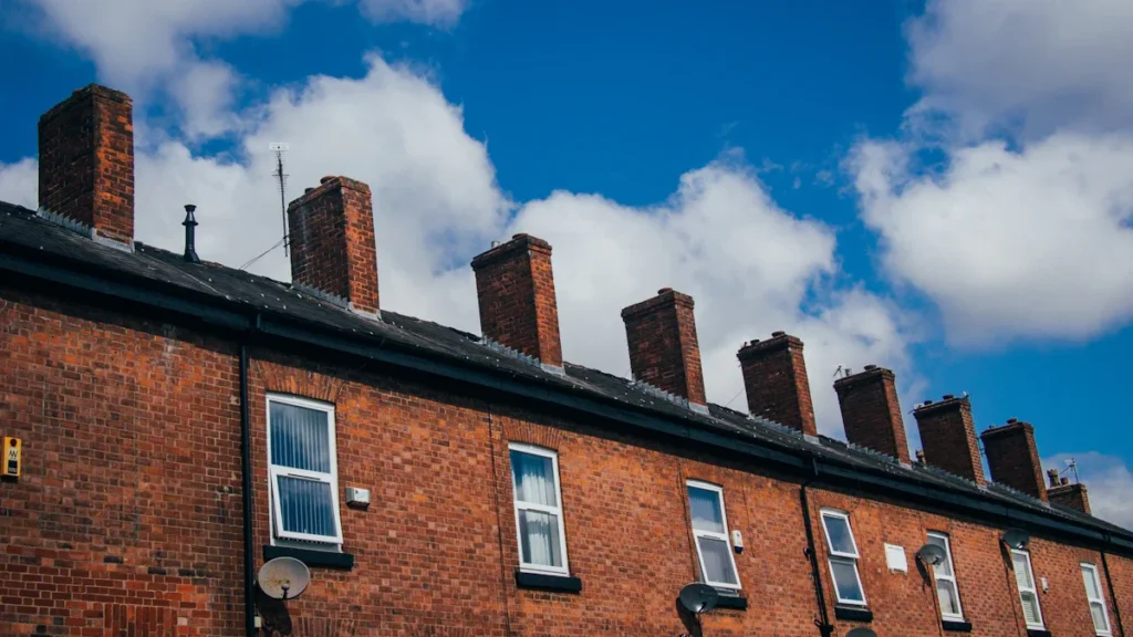 A row of traditional red-brick terraced houses in Chorlton, Manchester, under a bright blue sky.