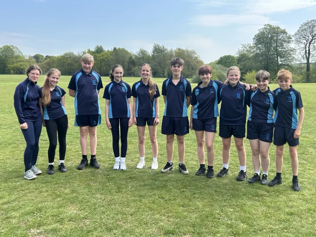 Ten students in blue and navy sports uniforms standing together on a grassy field outside.