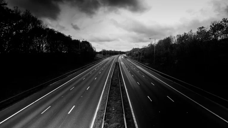 A grayscale photograph of a wide, empty multi-lane motorway in Manchester under a dramatic, cloudy sky.