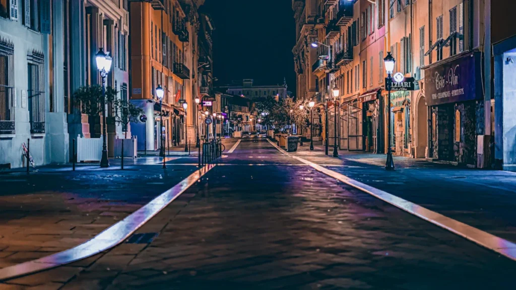 An empty European city street at night with glowing street lamps and historic apartment buildings.