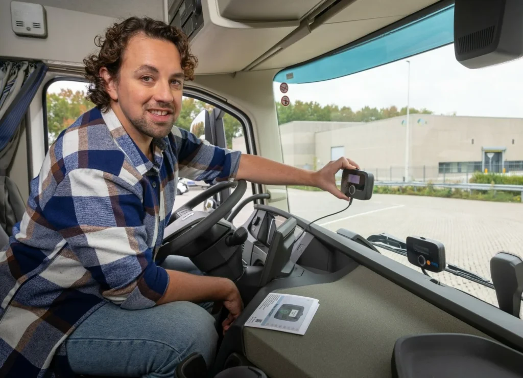 A man in a plaid shirt installs an electronic device on a truck windshield inside the cabin.