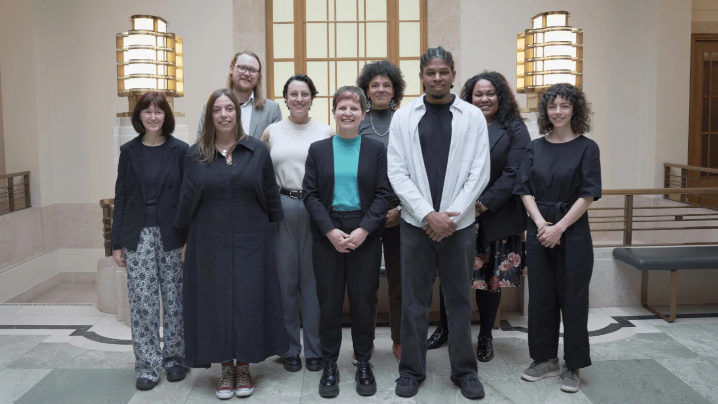 A group of nine diverse professionals standing together and smiling in a brightly lit architectural atrium.