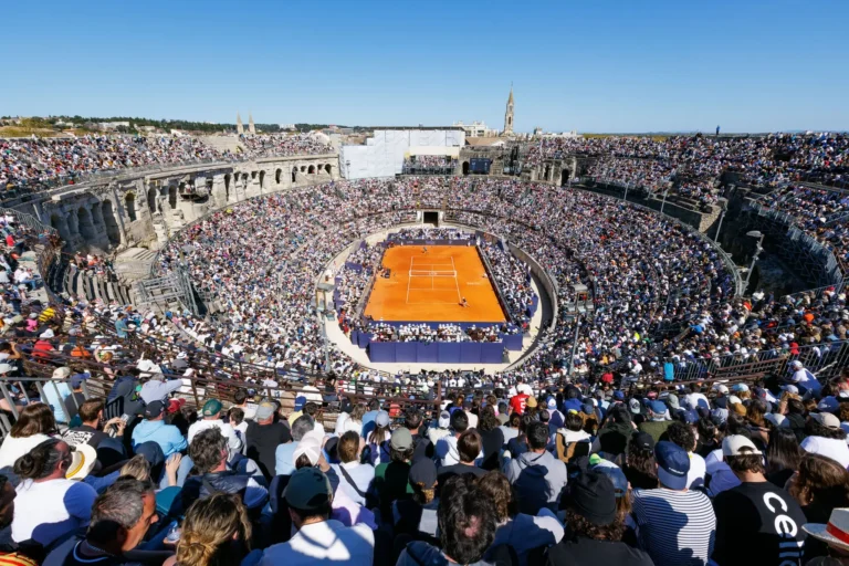 A clay tennis court inside a packed ancient Roman amphitheater under a clear blue sky.