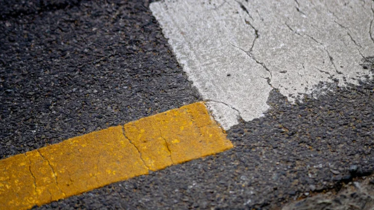 A high-detail close-up of fresh asphalt pavement with crisp white and yellow road markings.