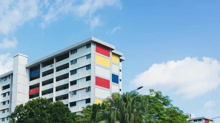 A modern high-rise social housing apartment block featuring colorful yellow, red, and blue exterior panels against a bright blue sky.