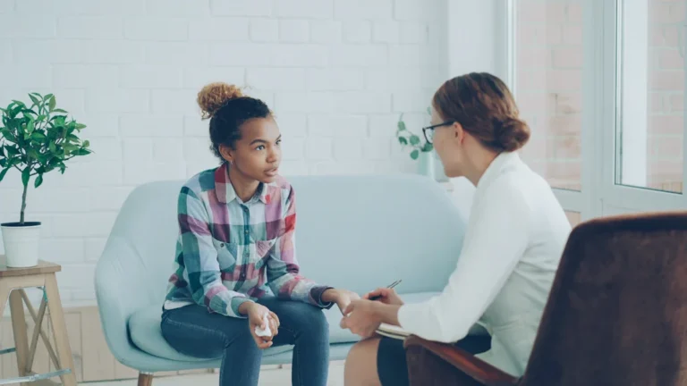 A young woman in a counseling session holding a tissue while talking to a healthcare professional.