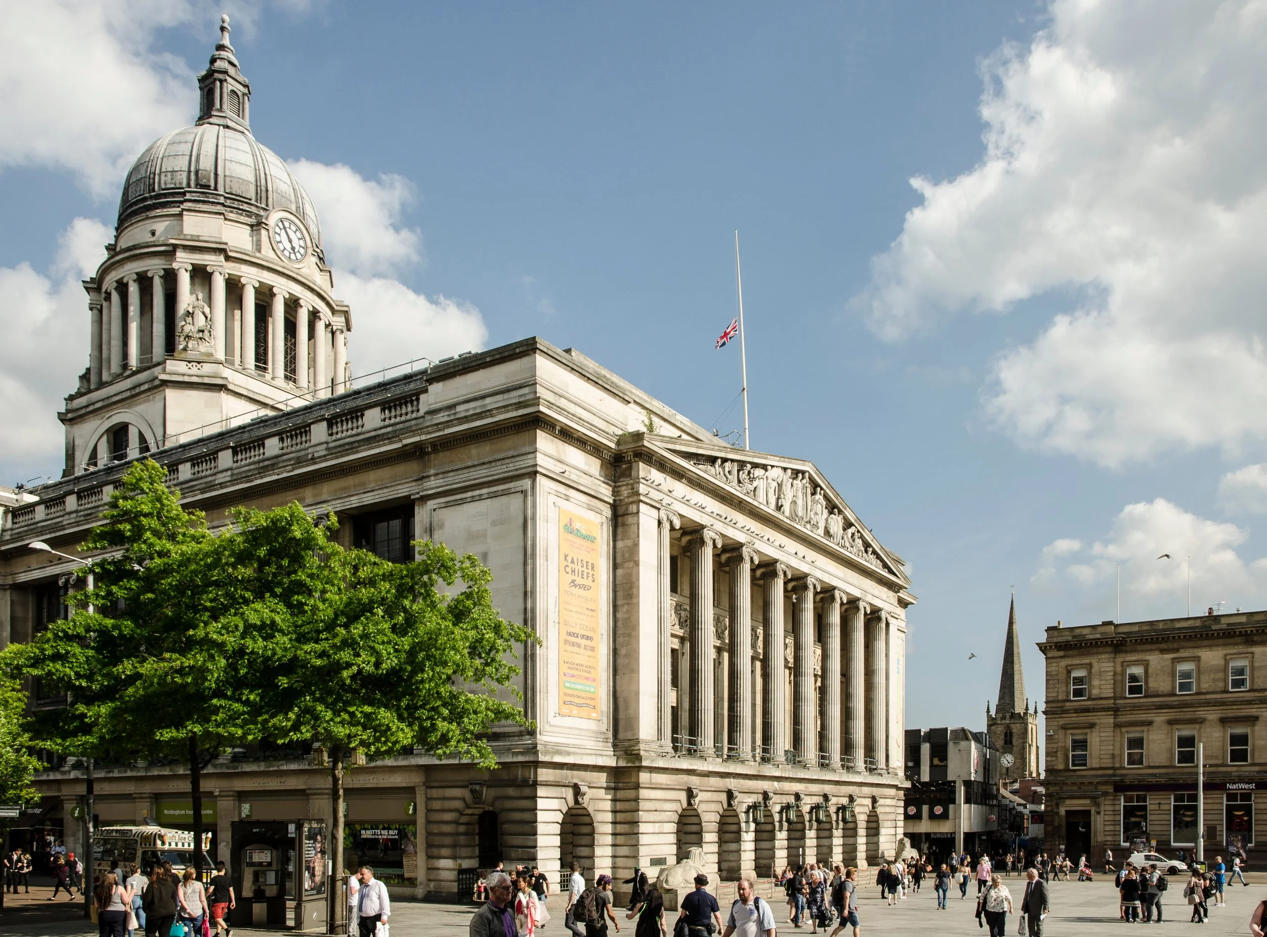 Neoclassical building with a clock tower dome and columns under a blue sky with pedestrians below.