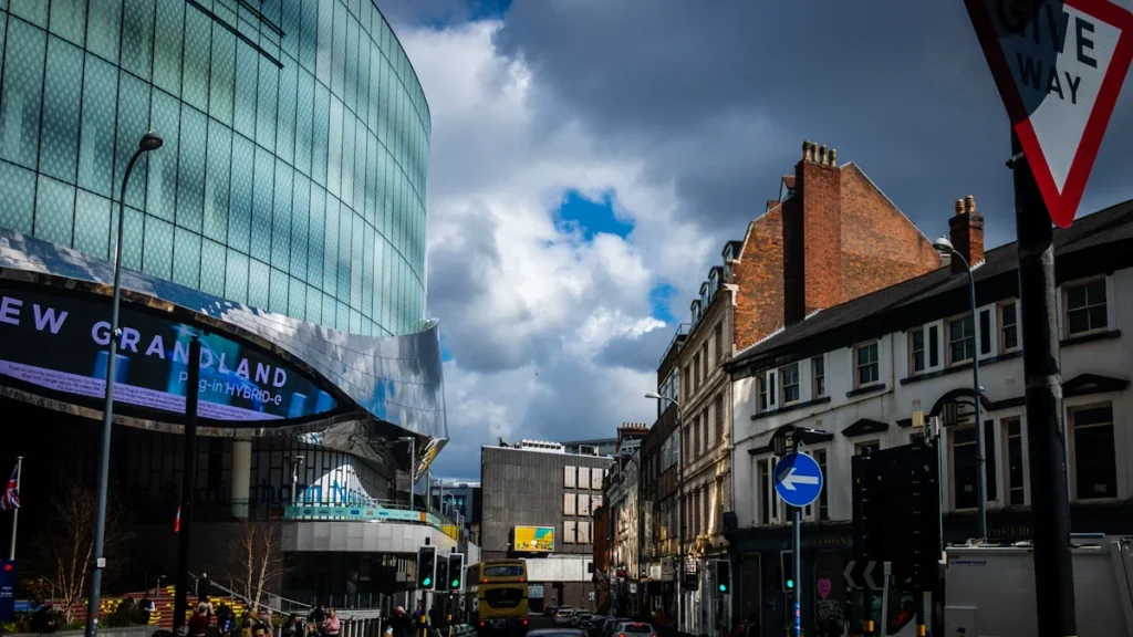 A view of Nottingham city centre featuring the modern curved glass facade of the Victoria Centre alongside traditional brick architecture under a dramatic sky.