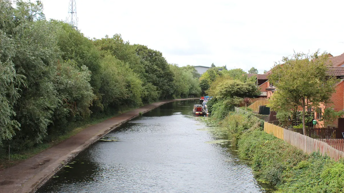 A calm canal winding through a suburban residential area with tree-lined banks in UK.