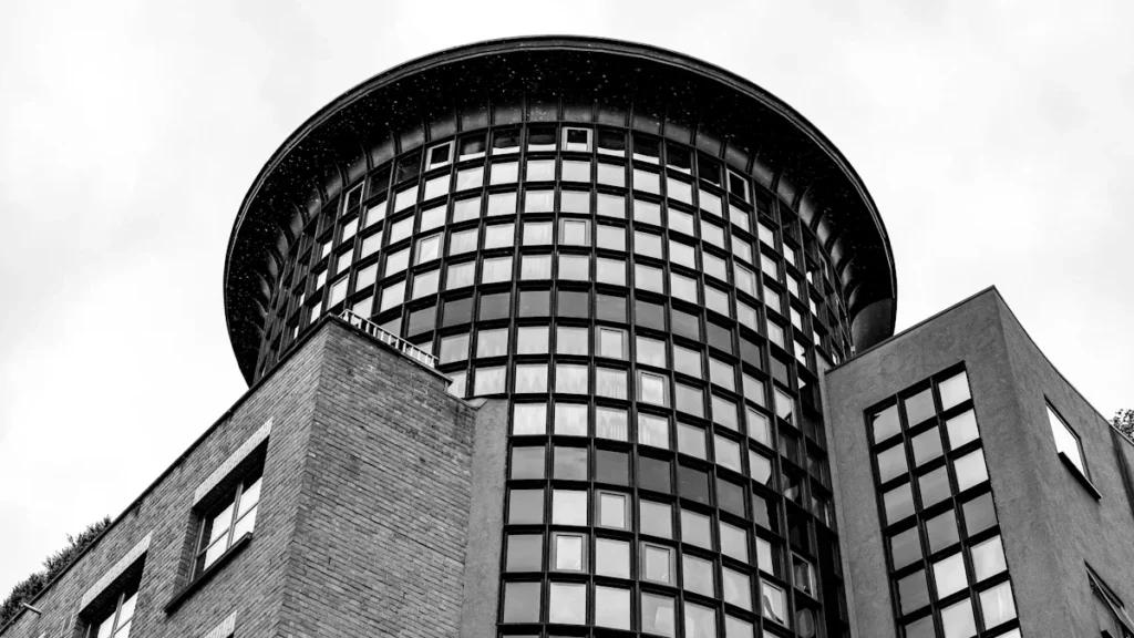 A low-angle black and white photograph of a modern circular brick and glass building in the UK.