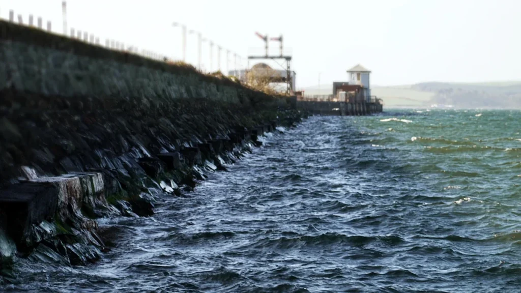 Waves crashing against a sturdy stone pier structure along a coastal embankment.
