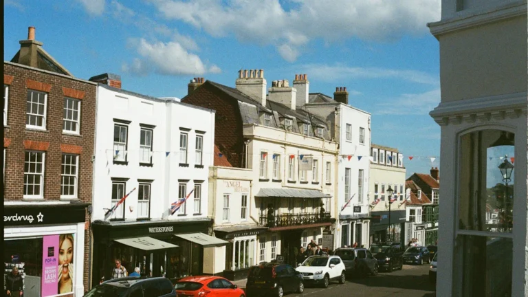 A sunlit street in a British town with traditional brick buildings and cars under a clear blue sky.