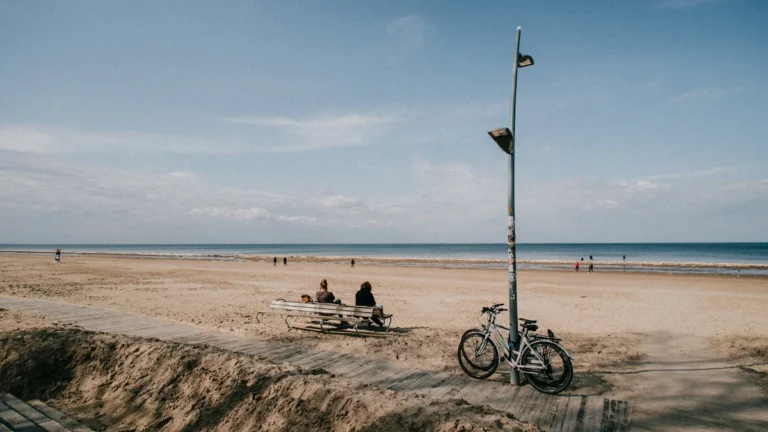 A wide sandy beach in Jurmala, Riga, featuring a wooden path, a parked bicycle, and visitors.