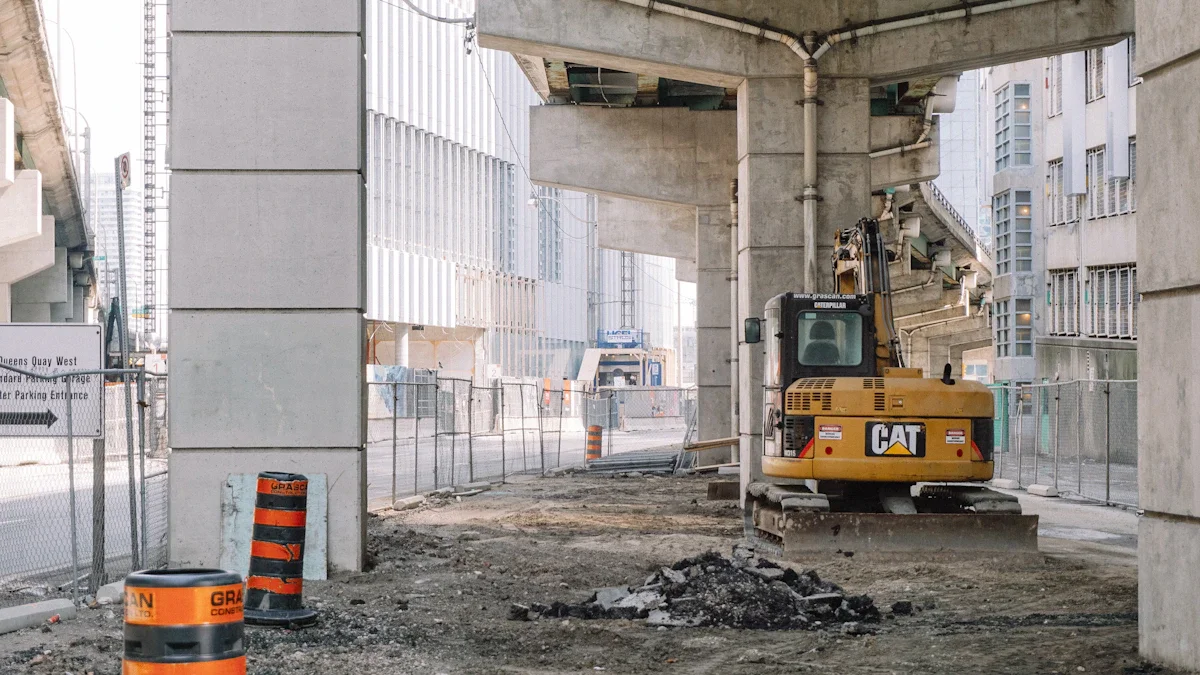 A yellow excavator parked at an urban construction site with orange traffic barrels and concrete structures.