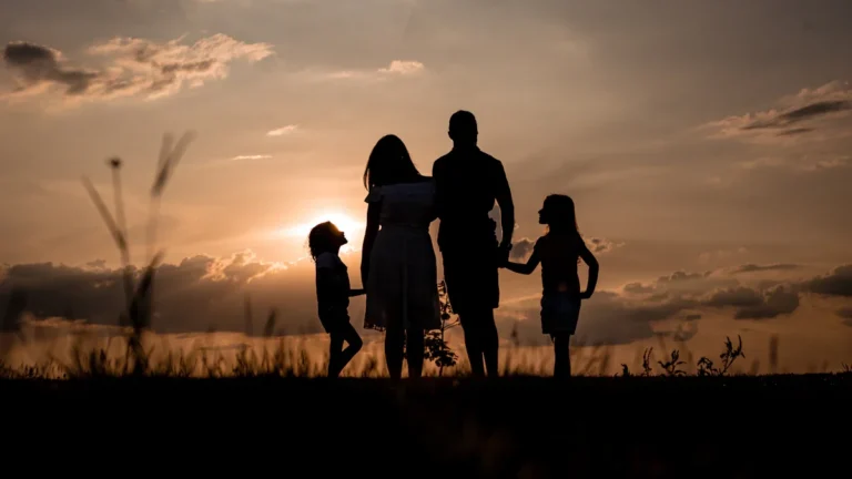 Silhouetted family standing in a field during a golden sunset, representing togetherness and support.