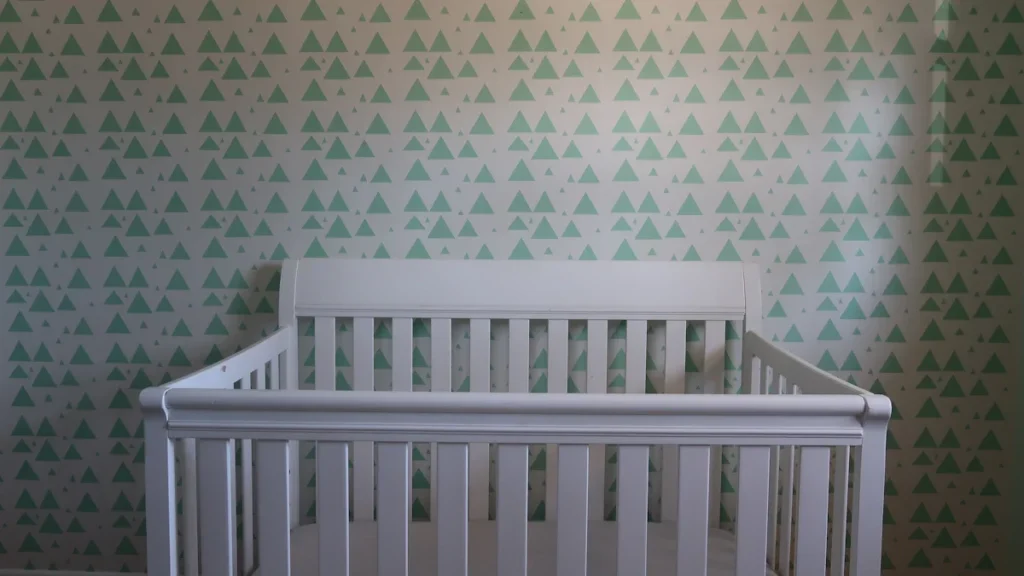 A clean, white wooden baby crib positioned against a green and white patterned wall.