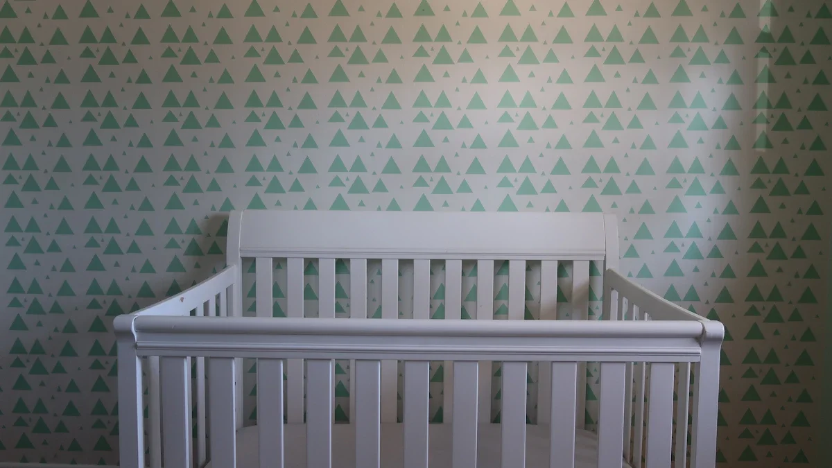 A clean, white wooden baby crib positioned against a green and white patterned wall.