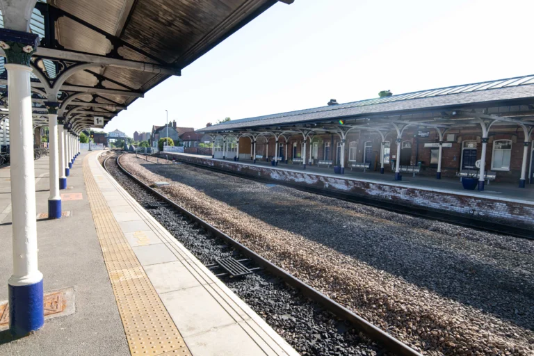 Empty railway station platforms under a clear sky with tracks curving toward a distant bridge.