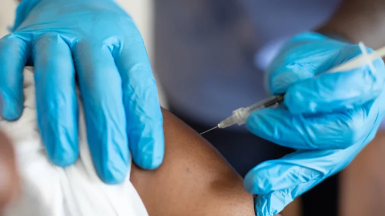 A healthcare professional wearing blue gloves administers a vaccine booster to a resident's arm.