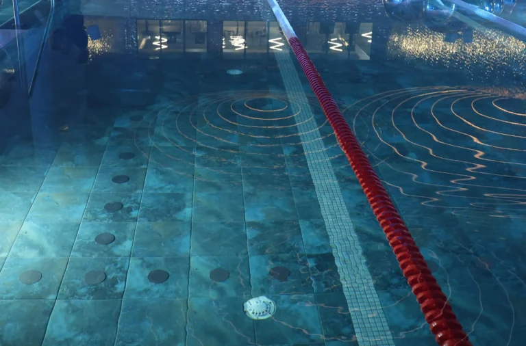 Blue indoor swimming pool with a red lane rope and circular ripples on the water's surface.