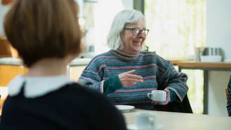 Two women engaging in a natural conversation over coffee in a bright community setting.