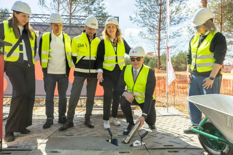 People in hard hats and safety vests watch a man place a time capsule into the ground.