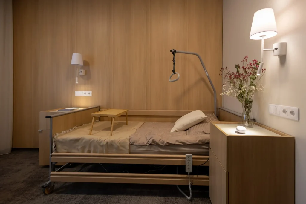 Modern adjustable wooden patient bed in a warm, wood-paneled room with a trapeze bar overhead.