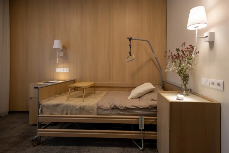 Modern adjustable wooden patient bed in a warm, wood-paneled room with a trapeze bar overhead.