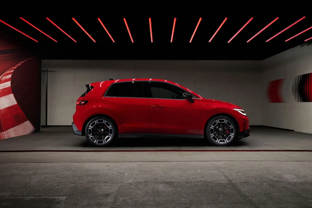 Side profile of a red compact hatchback in a dark studio with red linear ceiling lights.