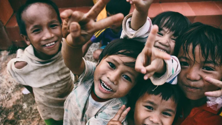 Group of young children smiling and giving peace signs to the camera
