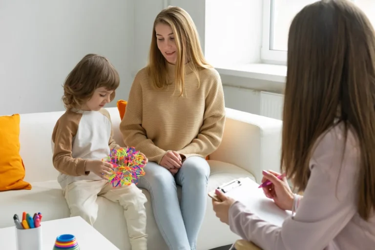 Mother and child sit on a sofa while a specialist takes notes during a consultation.