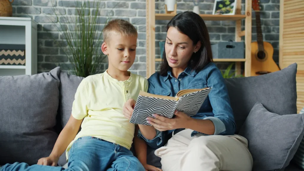 A woman and a young boy sitting together on a sofa reading a book in a cozy living room.
