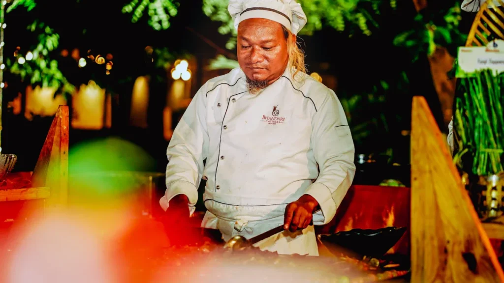 A chef in a white uniform works with focus under warm, stage-like lighting, capturing the theatrical essence of the play about Mārtiņš Rītiņš.
