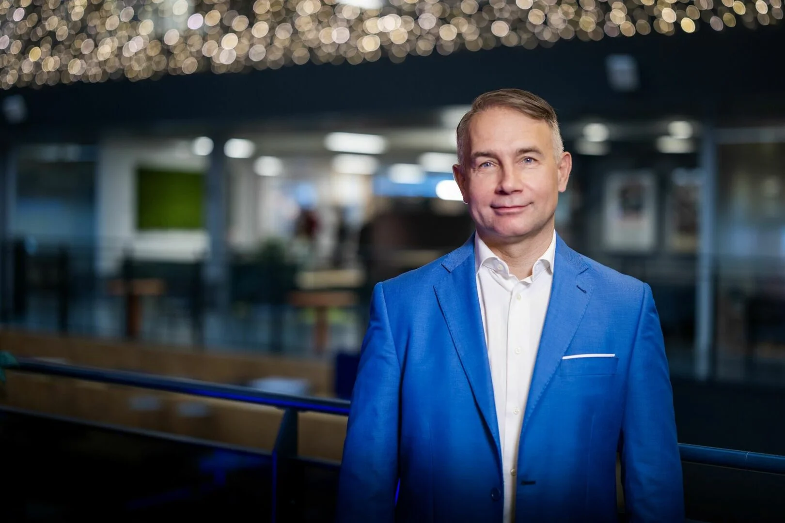 Man wearing a bright blue suit jacket and white shirt in a modern, blurred office setting.