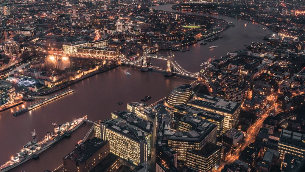 An expansive aerial view of a UK city skyline at dawn, featuring a river and bridges.