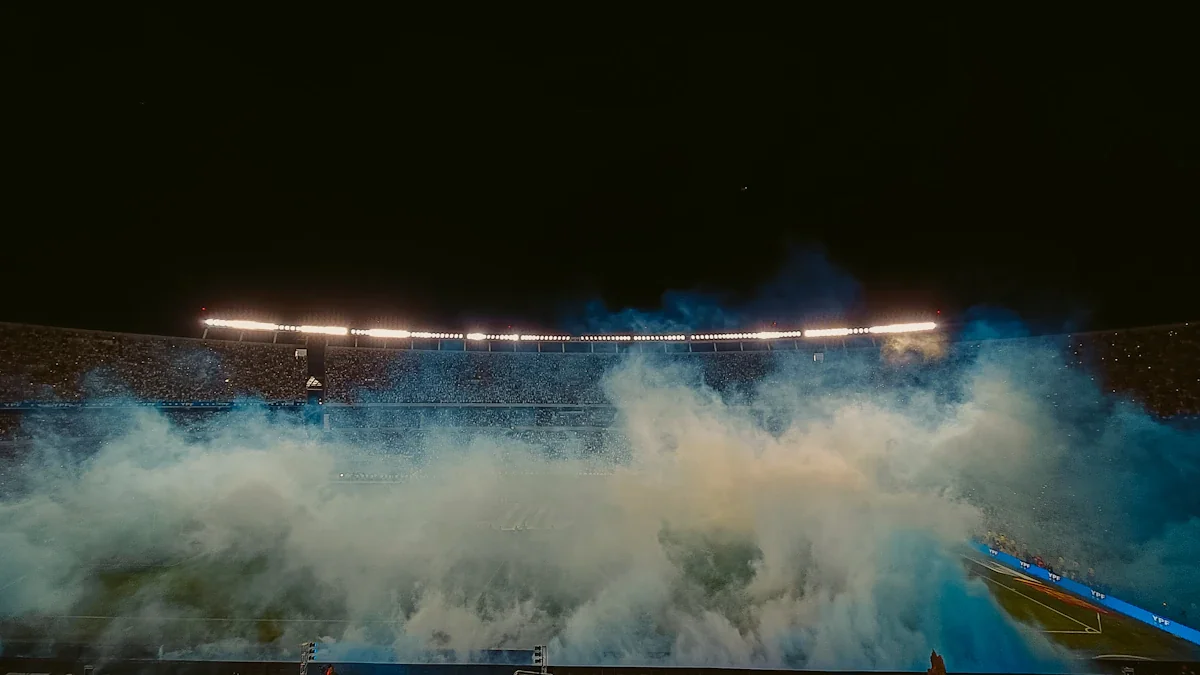 A football stadium illuminated at night with thick blue smoke rising from the field.