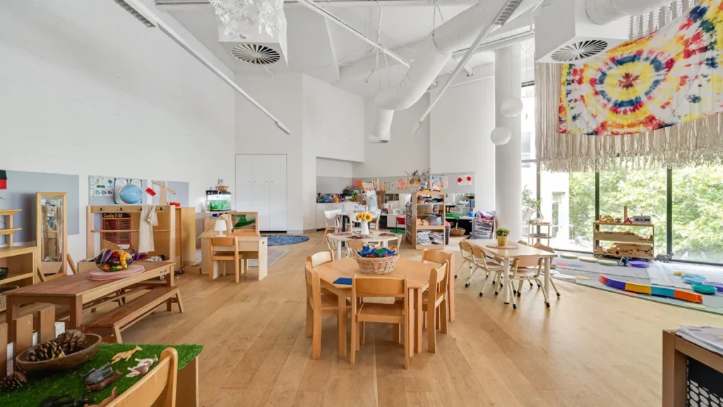 Spacious, modern, light-filled educational interior with natural wood furniture and large windows.
