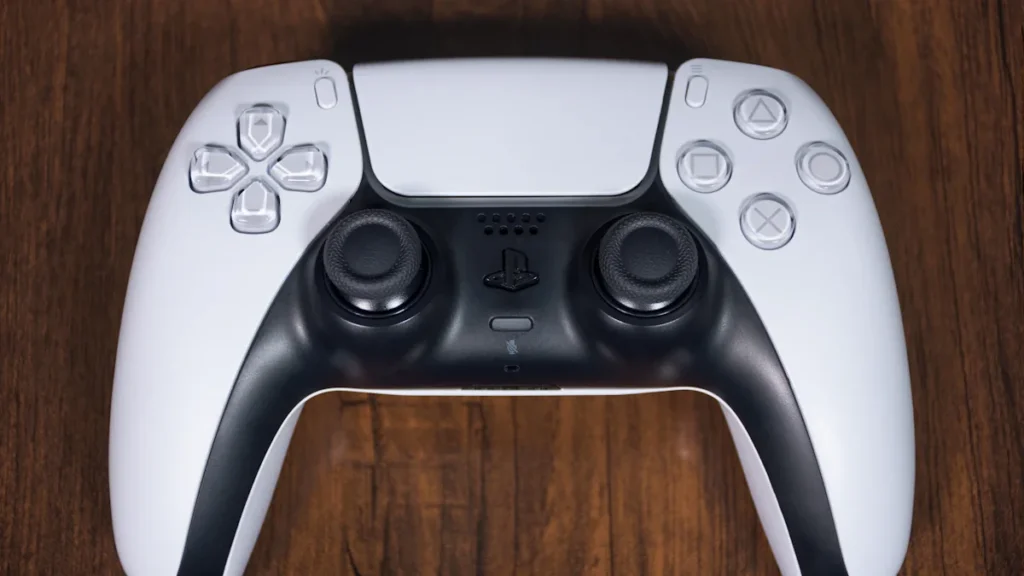 A standard white PlayStation 5 DualSense controller resting on a dark wooden desk surface.
