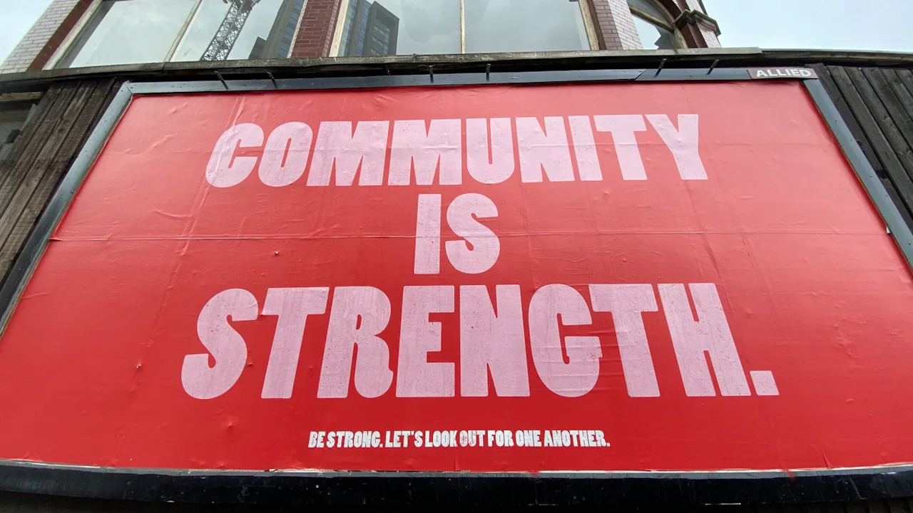 A red billboard stating Community is Strength in a London urban environment.
